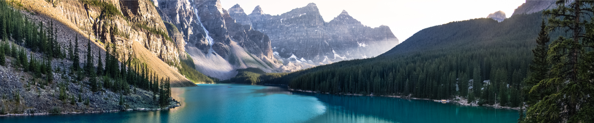 Blue stream of water surrounded by green forestry on the right side and the bottom of a rocky grey mountain on the left side