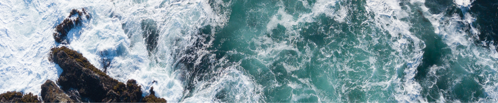 Greenish-Blue body of water with waves hitting dark brown rock 