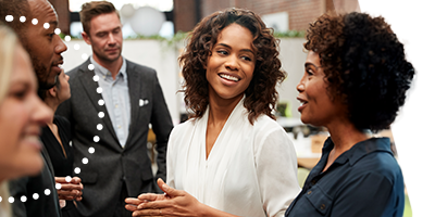 Four people standing together, smiling and holding notebooks, conversing at an indoor event.